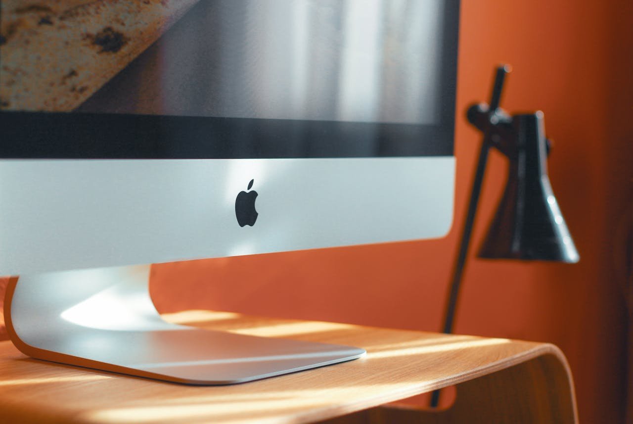 A sleek computer and stylish desk lamp on a wooden table in a modern workspace.